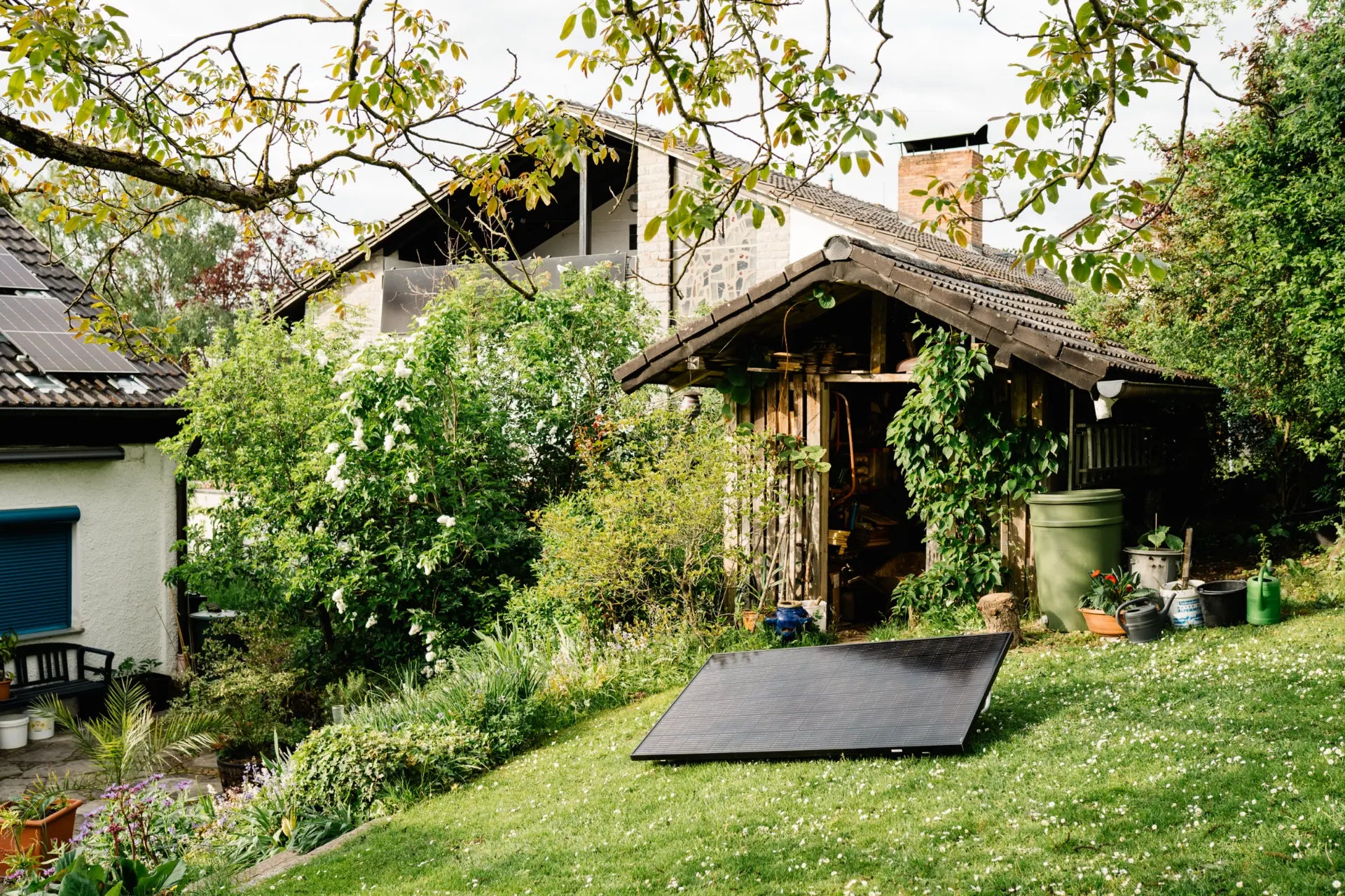 Solarmodul auf Gartenfläche mit Gartenhaus und Haus im Hintergrund